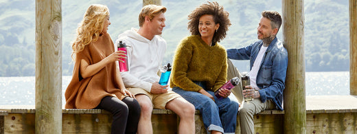 Two men and two women chatting while sat on a jetty in the Lake District with Thermos water bottles