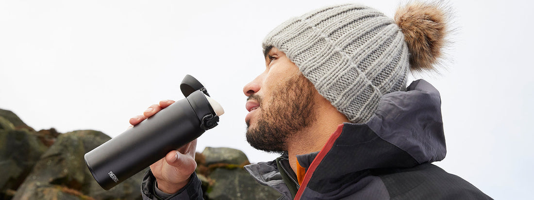 A male hiker wrapped up warm drinking from his Thermos Water Bottle