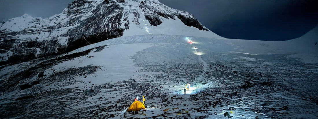 Mount Everest lit up by the stars. From a distance a small team of climbers trek to the summit with head torches on