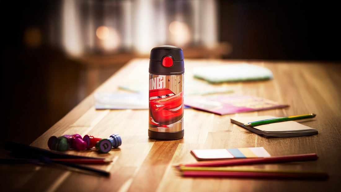 A Thermos Disney FUNtainer water bottle sat on a dining table with children's colouring pens and books scattered around