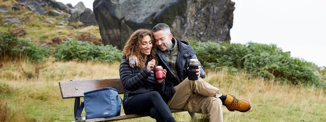 A happy couple sat on a bench at Ilkley Moor eating from Thermos Food Flasks