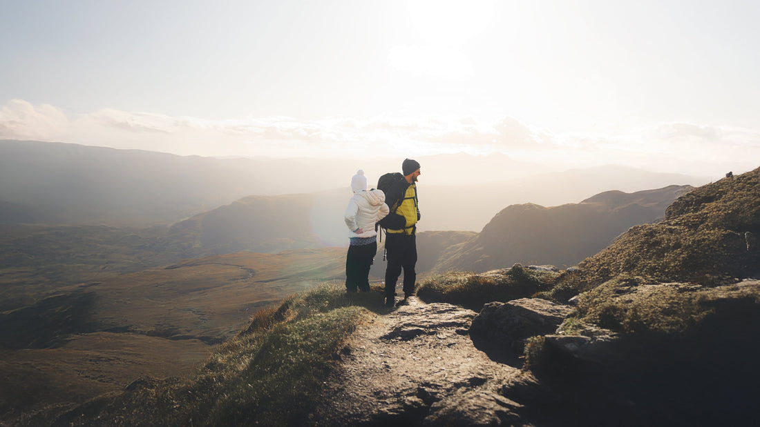 Two hikers standing on a scenic mountain trail, overlooking rolling hills and a breathtaking sunrise. Outdoor adventure, UK hiking, and nature exploration