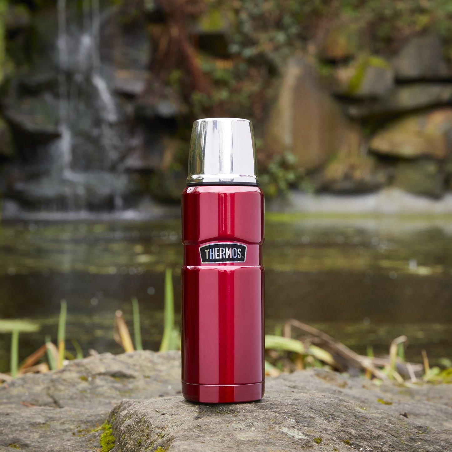 Red 470ml STAINLESS KING FLASK on a rock with a waterfall in the background