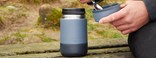 A male hand shot eating from a Thermos Food flask with the countryside in the background