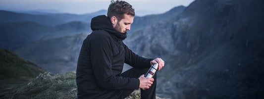 A male hiker about to open his Thermos Flask for a hot drink with a stunning backdrop of stunning high hills and rock faces