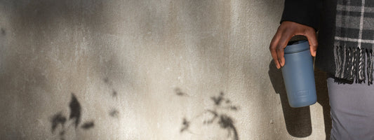 A man holding a Thermos Travel Mug next to a wall with plants growing nearby