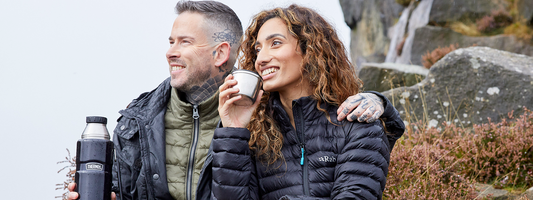 A happy couple on a day out in the countryside drinking hot drinks from a Thermos Flask