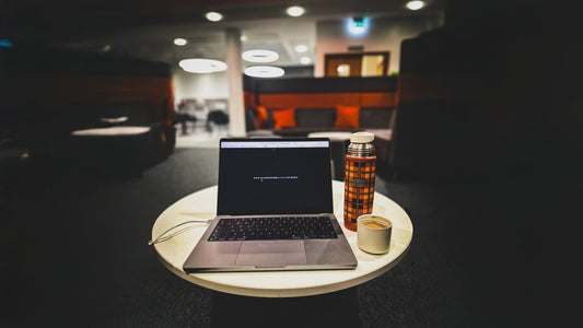Laptop open with headphones plugged in and a thermos flask of tea on a desk in a university library
